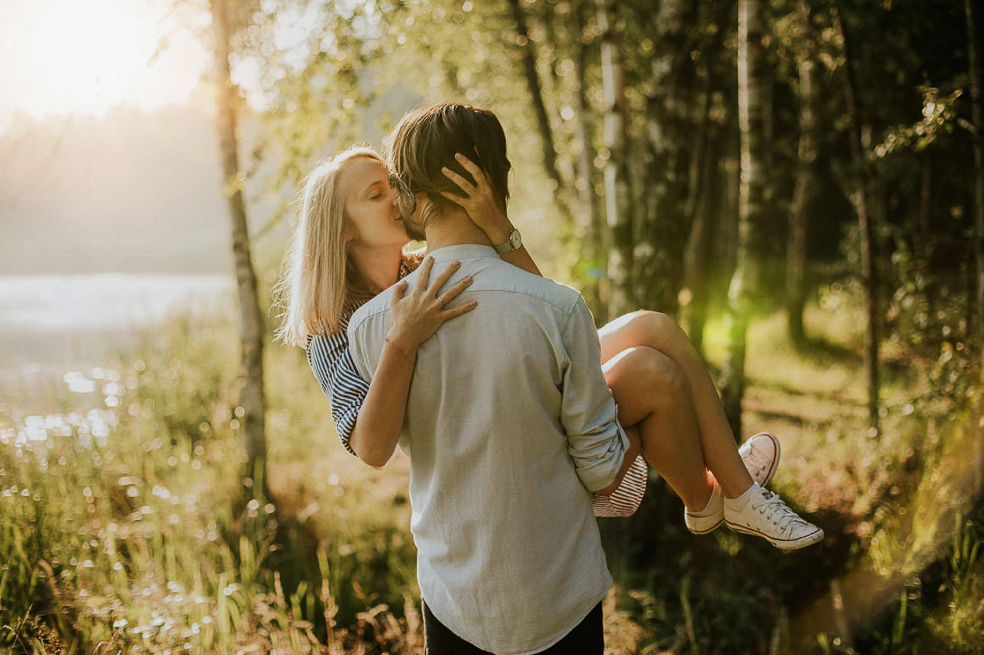 Para w lesie, mężczyzna trzyma kobietę na rękach.