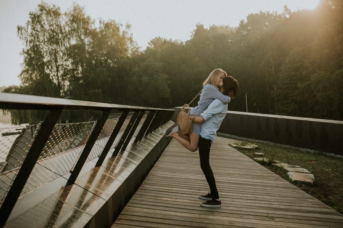 Para całująca się na drewnianym pomoście o zachodzie słońca.