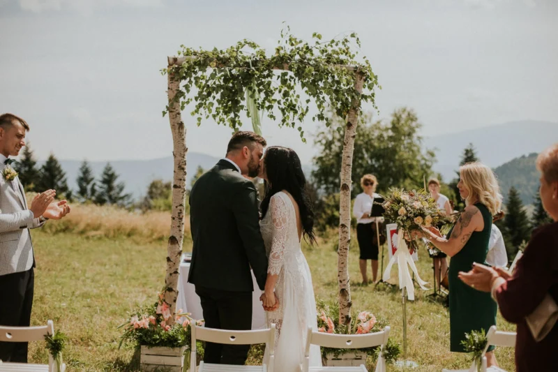Para młoda całuje się na ceremonii ślubnej na zewnątrz.