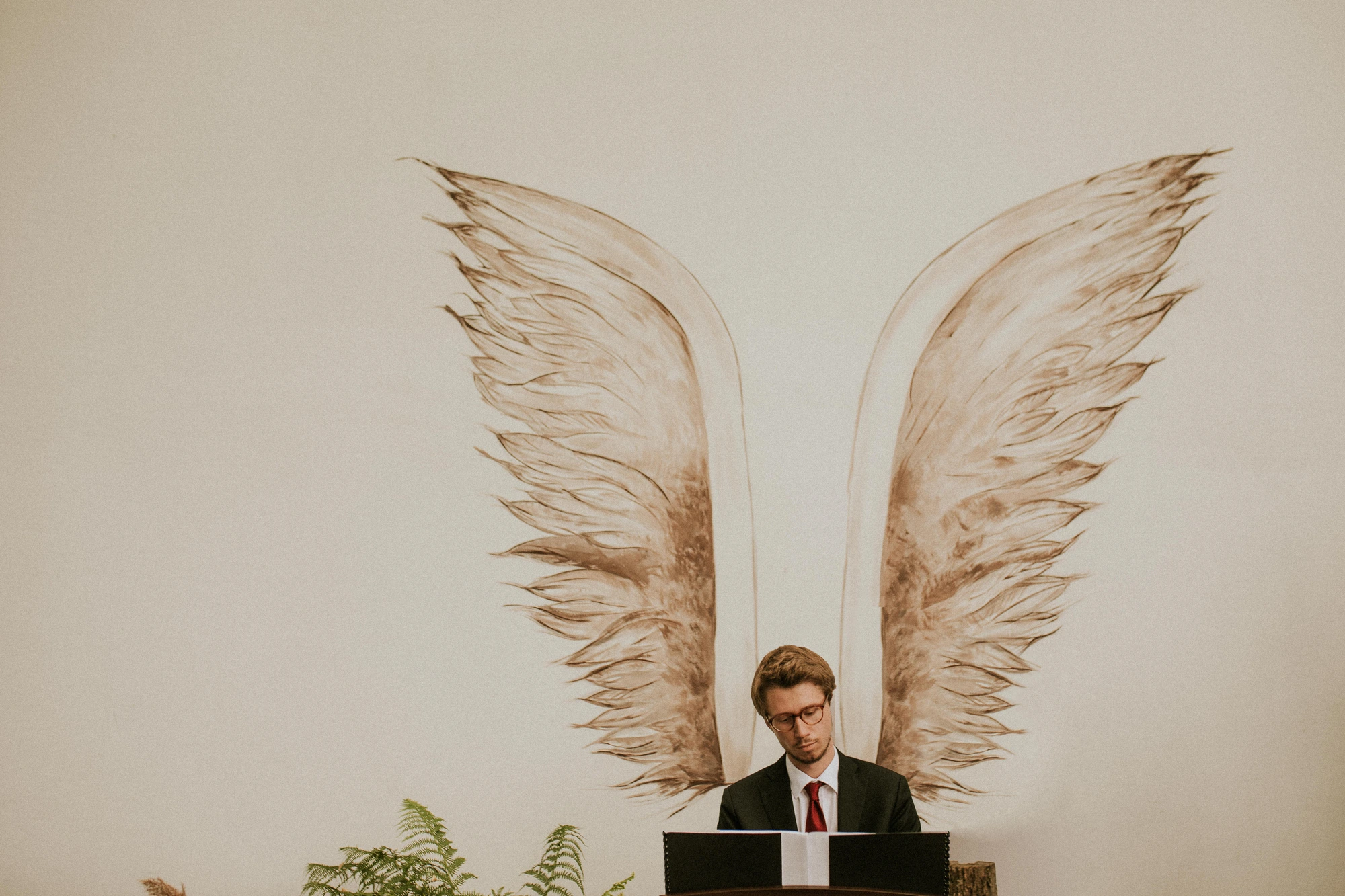 Mężczyzna w garniturze, anielskie skrzydła na ścianie.