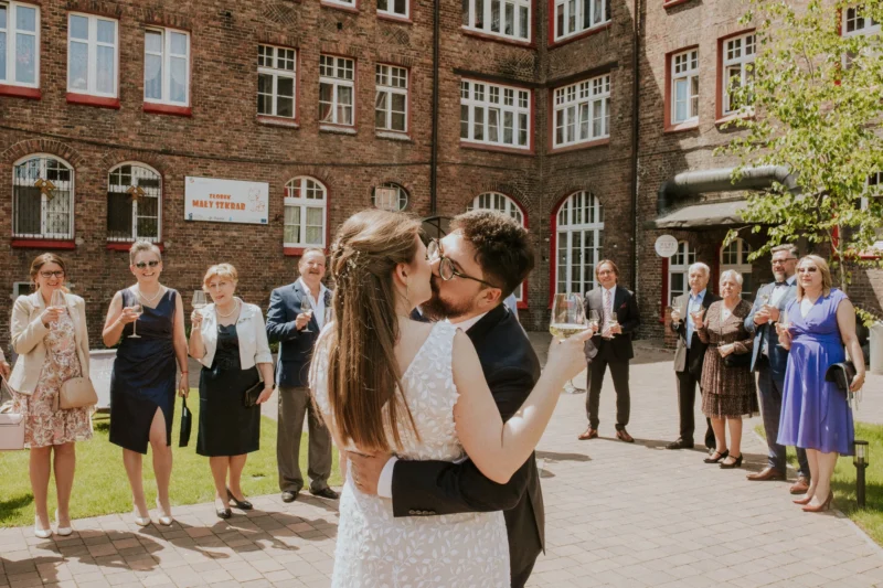 Para młoda otoczona weselnymi gośćmi przed budynkiem.