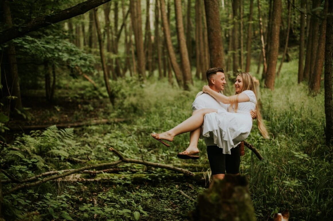 Para w lesie, mężczyzna trzyma kobietę na rękach.