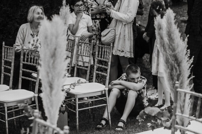 Chłopiec siedzi na ziemi wśród gości na weselu.