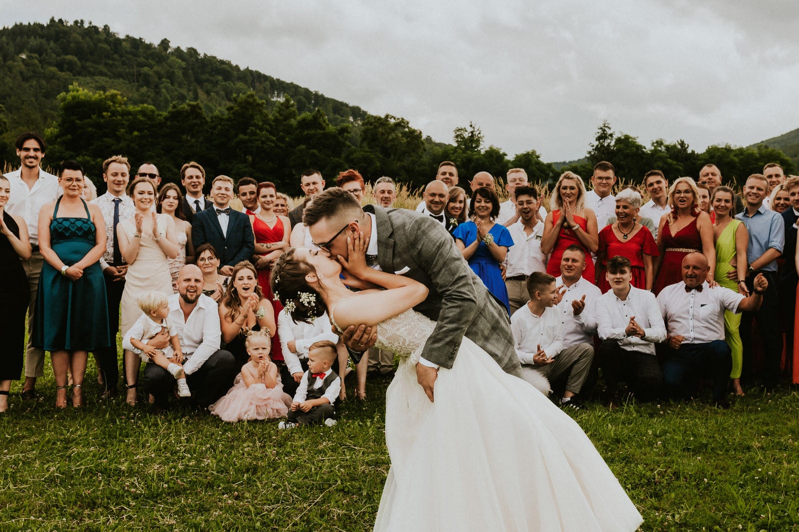 Para młoda całuje się na tle gości weselnych.