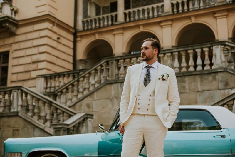 Mężczyzna w eleganckim garniturze przed zabytkowym budynkiem.