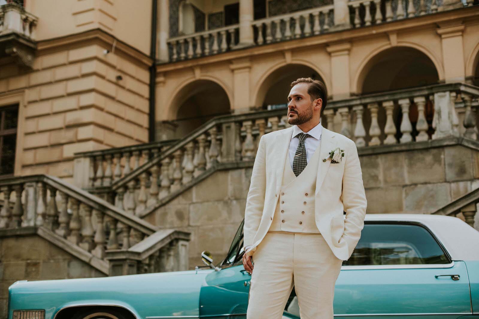 Mężczyzna w eleganckim garniturze przed zabytkowym budynkiem.