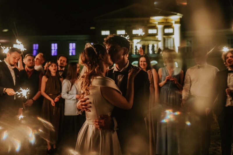 Para młoda całuje się, otoczona gośćmi z zimnymi ogniami.