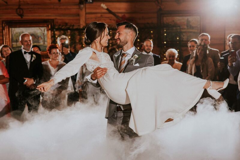 Para młoda tańczy na weselu wśród gości.