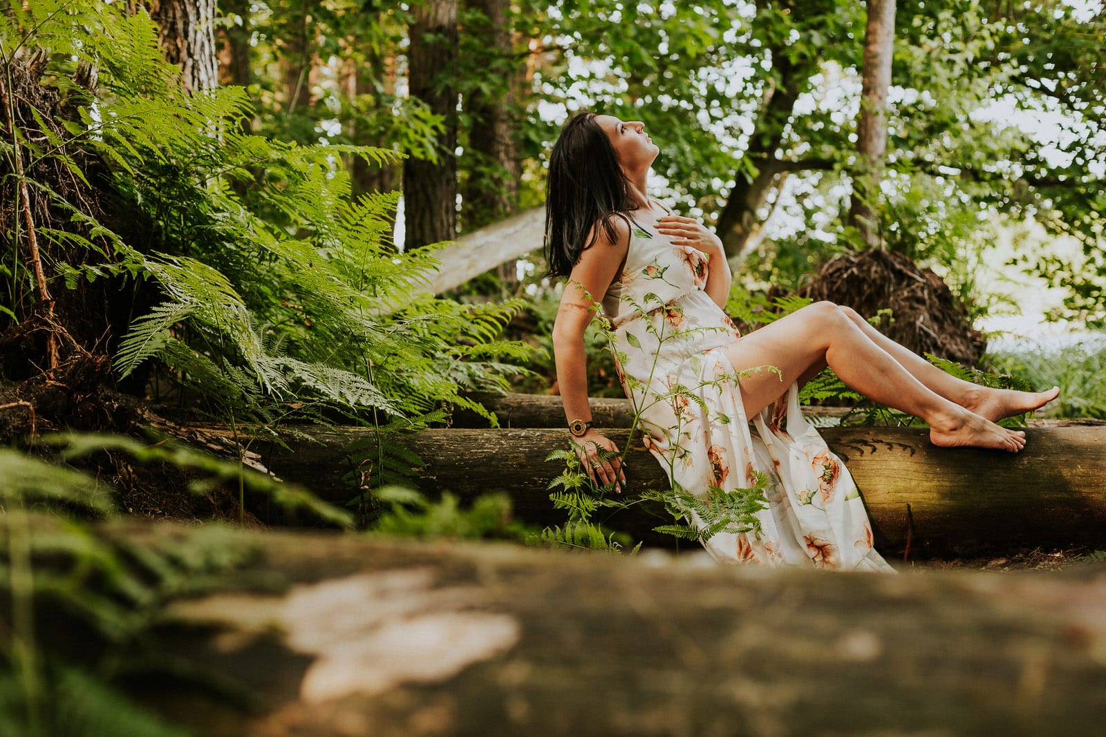 Kobieta w lesie na pniu drzewa, letnia sukienka.