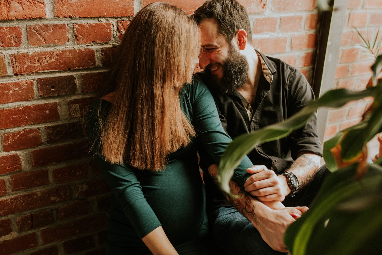 Para siedzi blisko siebie przy ceglanej ścianie.