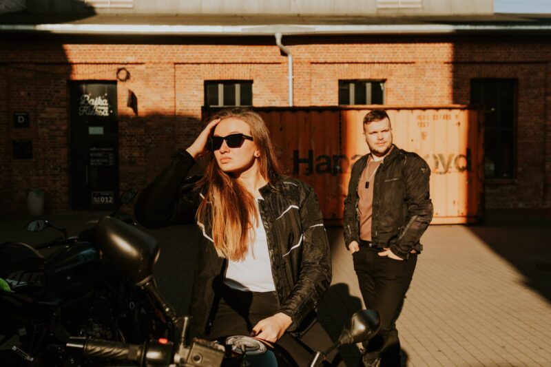 Dwoje ludzi w kurtkach motocyklowych stoi przed budynkiem.