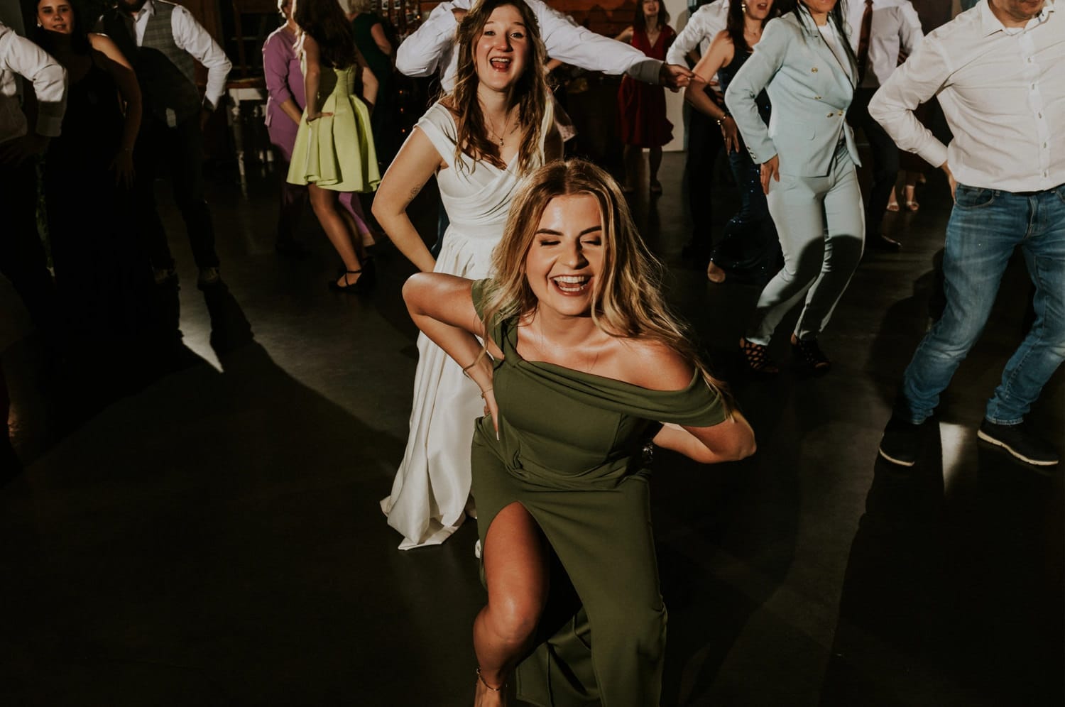 Tańczące osoby na weselu, uśmiechnięte kobiety w sukienkach.