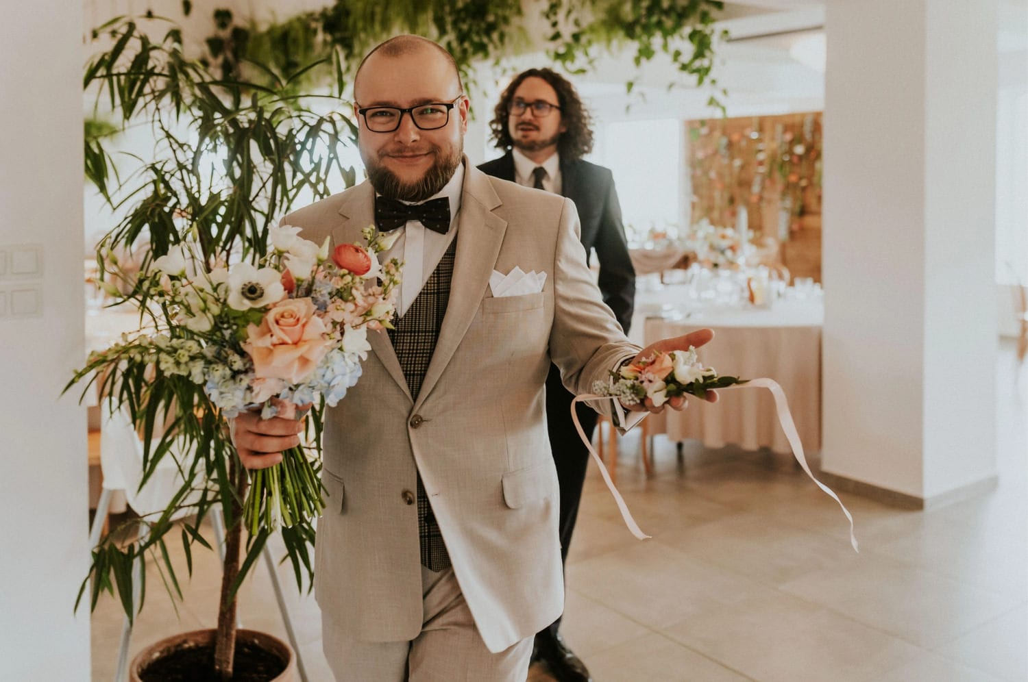 Mężczyzna w garniturze trzyma bukiet kwiatów podczas wesela.
