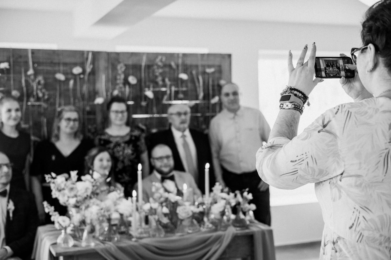 Osoba fotografuje grupę ludzi na uroczystości przy stole.