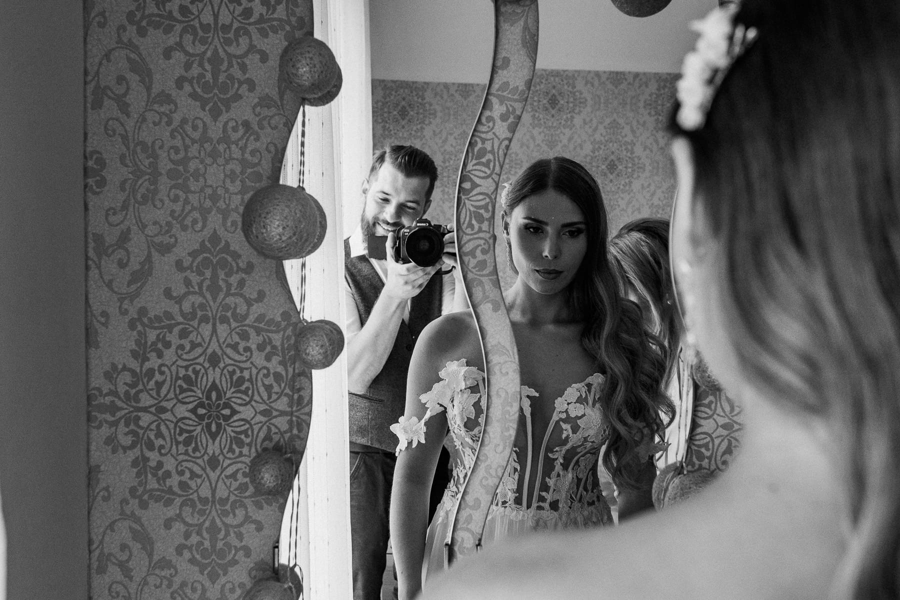 Kobieta w sukni ślubnej przed lustrem, fotograf w tle