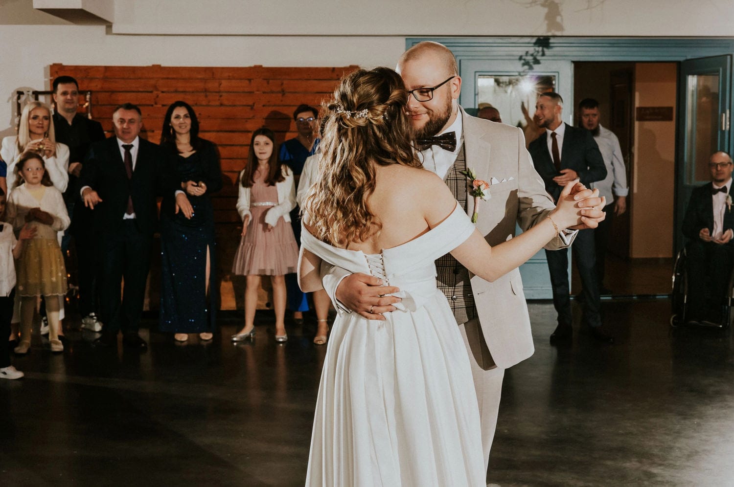 Para młoda tańczy na weselu, goście w tle.
