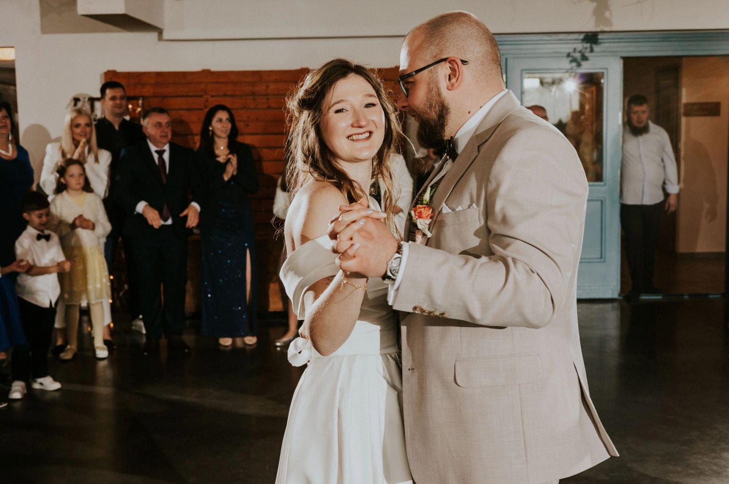 Para młoda tańczy na weselu, goście klaszczą.