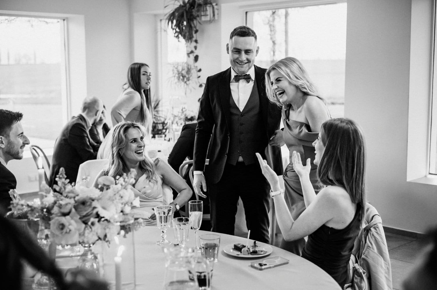 Goście na weselu śmieją się przy stole.