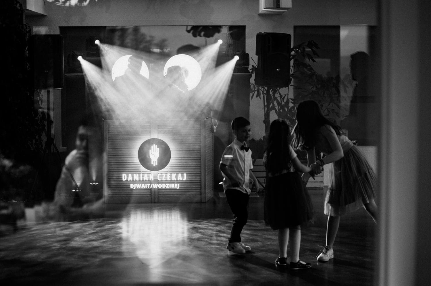 Czarno-biała scena z DJ-em i dziećmi tańczącymi.
