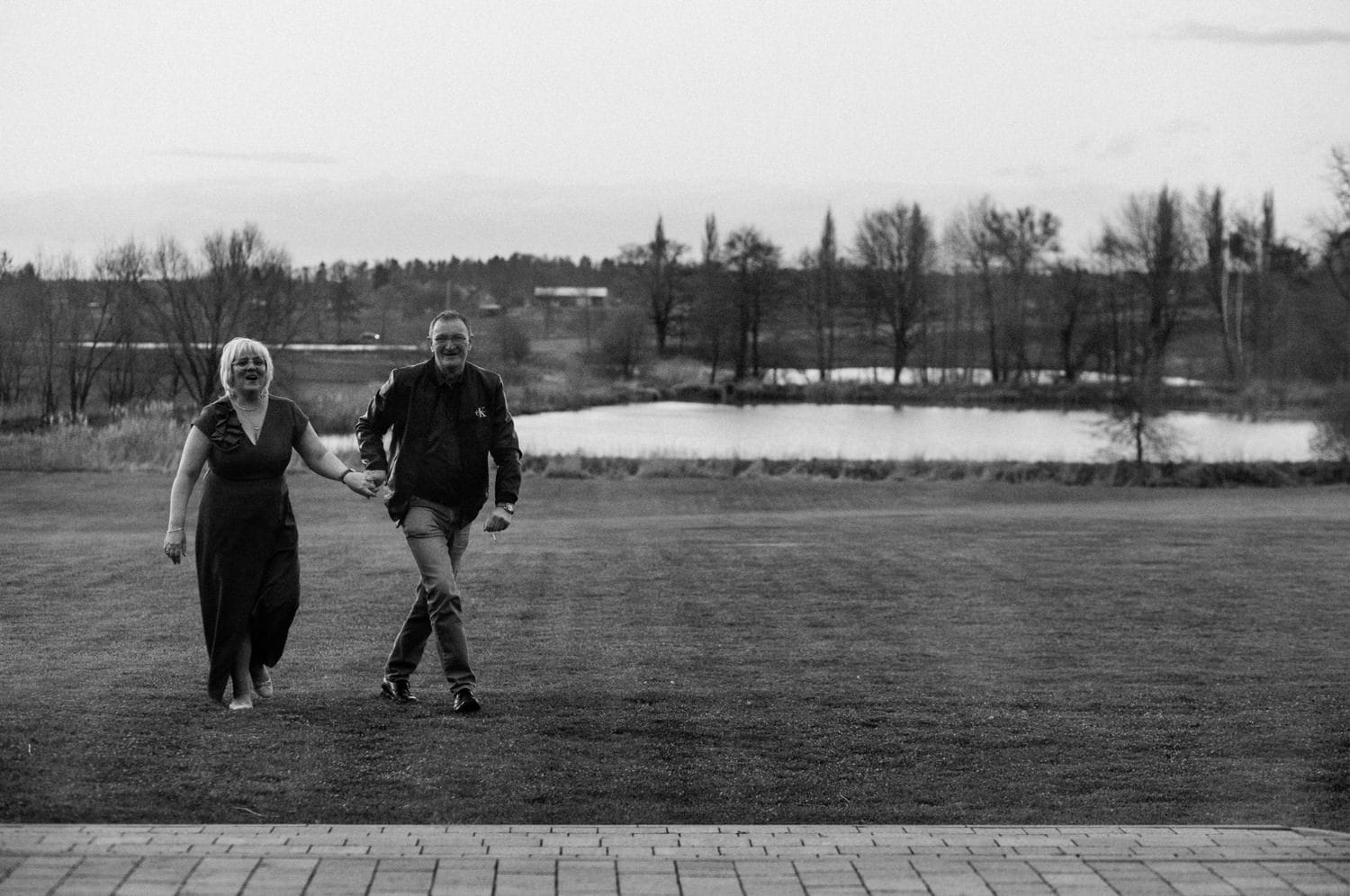 Para spacerująca po trawniku nad jeziorem.