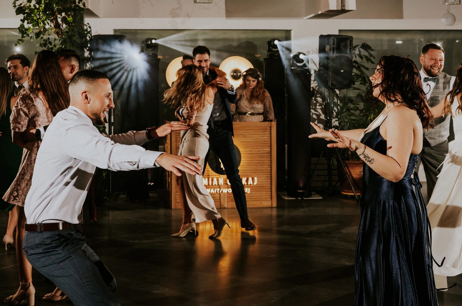 Tańczący goście na weselu, muzyka DJ, radość.