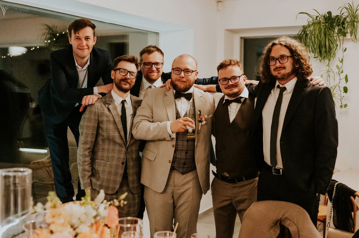 Sześciu mężczyzn w garniturach na przyjęciu weselnym.