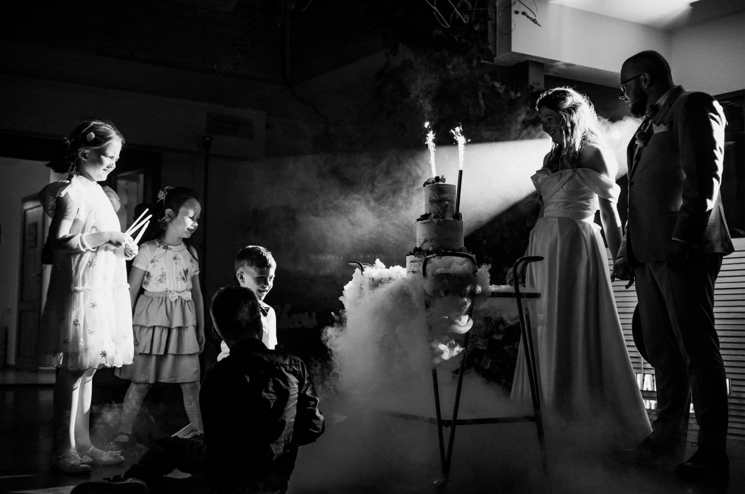 Dzieci podziwiają tort weselny w dymie i świetle.