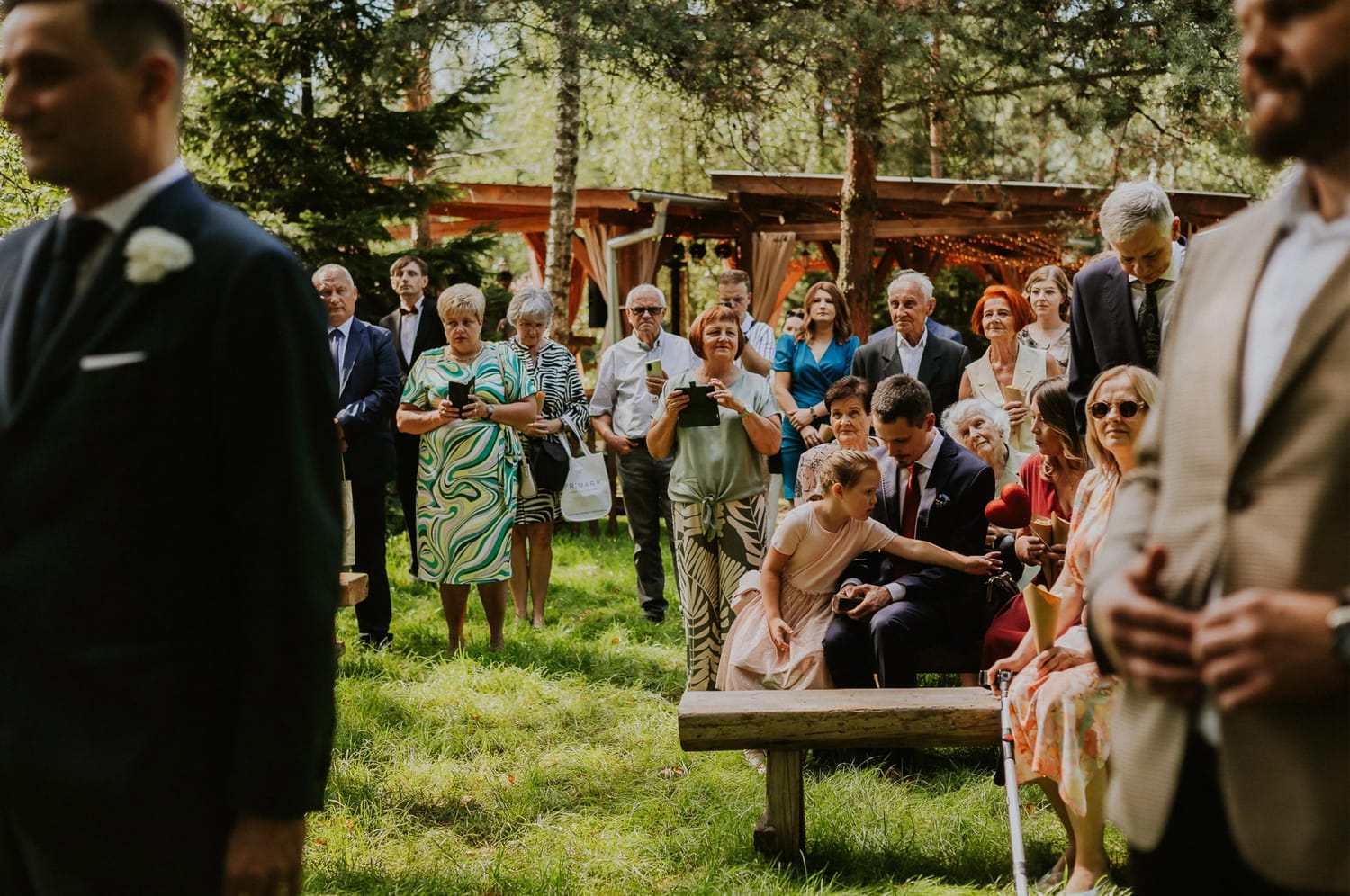 Uroczystość w ogrodzie, ludzie siedzą i stoją.