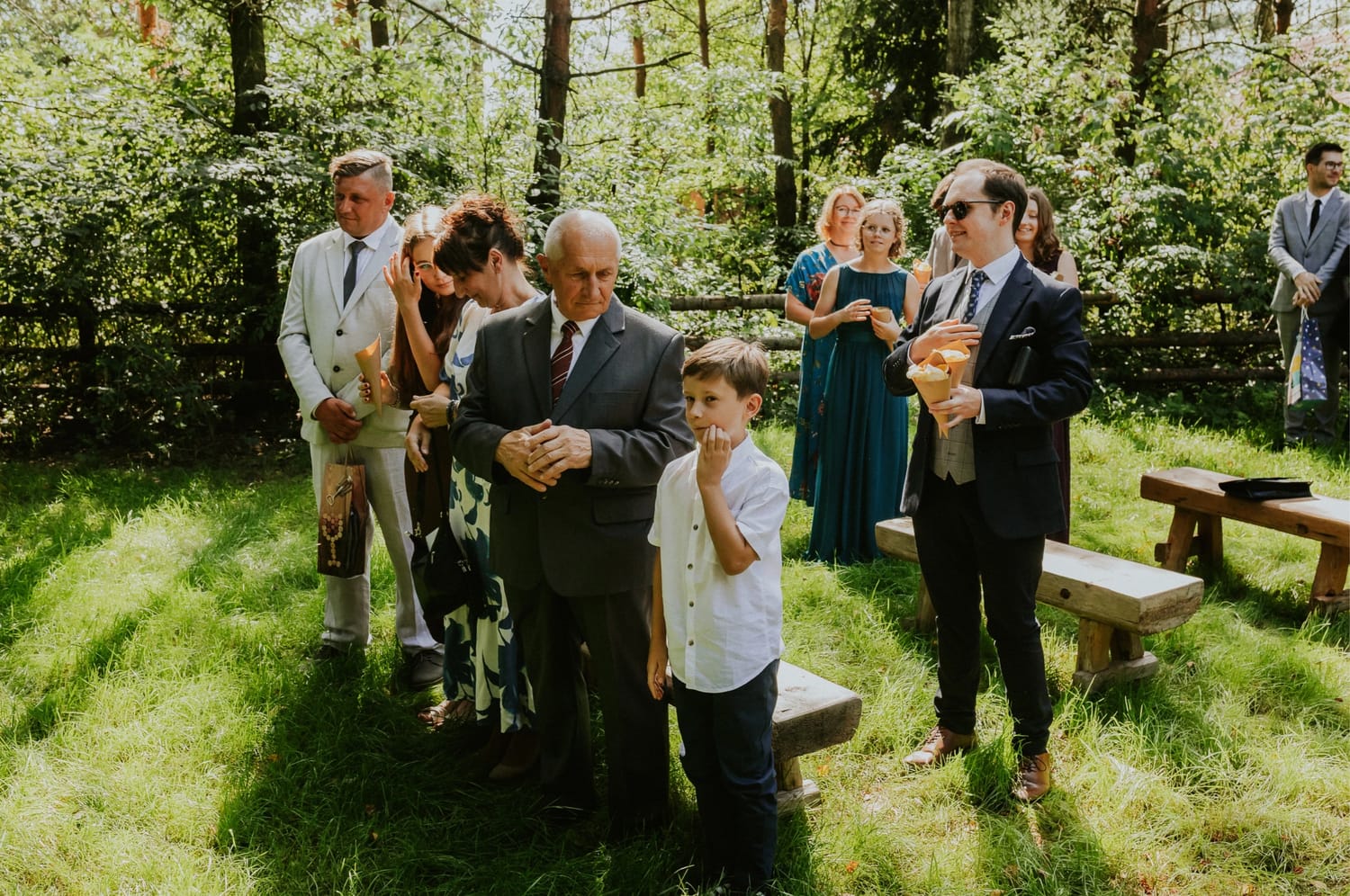 Ludzie w eleganckich ubraniach na zewnątrz, zielone otoczenie.