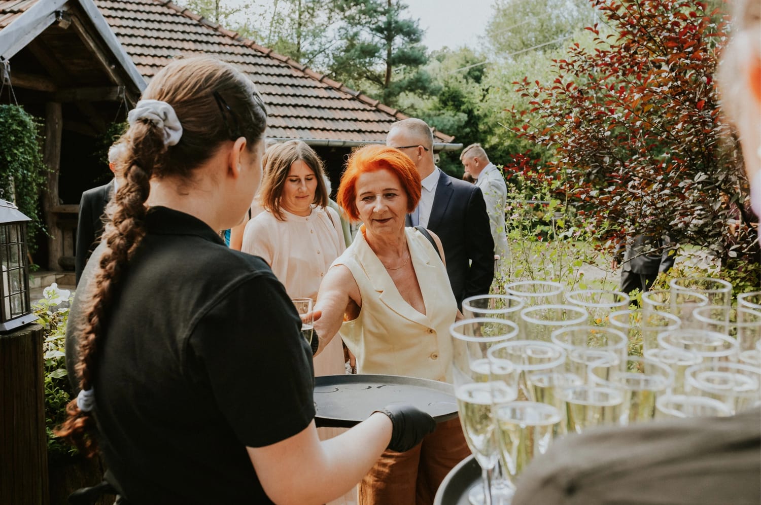 Goście przyjęcia biorą kieliszek szampana od kelnerki.
