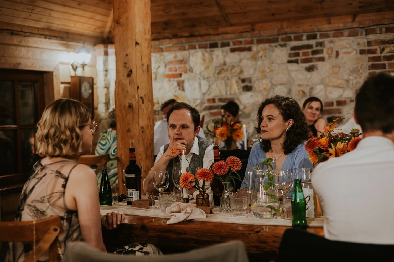 Ludzie przy stole w restauracji, kwiaty, drewniane wnętrze.
